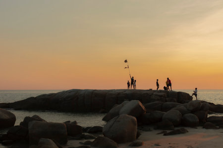The stones on beach in evening have the background of the sea and the evening sun. There are people standing on rocks and flagsの写真素材