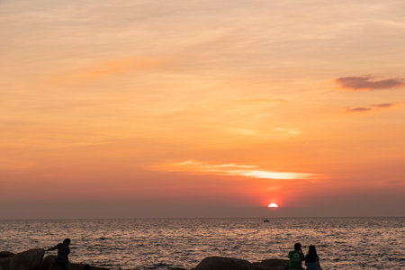 The sun on beach in evening have the background of the sea and the evening sun. There are people standing on rocks and flagsの写真素材