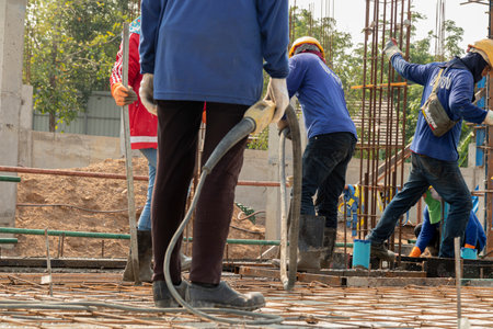 Workers put jeans on their feet holding concrete vibrators in their hands on rebar for pouring concrete in construction sites, columnar backgrounds and building conditions during construction.の写真素材