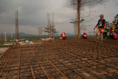 Blur red rusty on rebar  as structural steel for the floor to pour concrete, there is a background of workers tying wire to iron mountains and the sky are far away.の写真素材