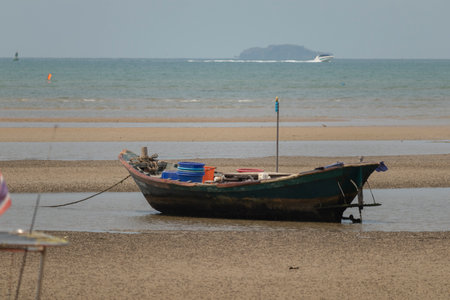fisherman's fishing boat on sand at a fishing village beach There is an island and sea background with the daytime sky. A stranded fishing boat After the sea has recededの写真素材