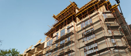 Panorama of a multi-storey residential building under construction and crane on a background of blue...