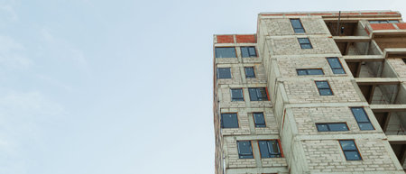 Panorama of a multi-storey residential building under construction and crane on a background of blue...