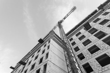 Black and white photo of a multi-storey residential building under construction and crane on a background of blue skyの写真素材