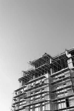Black and white photo of a multi-storey residential building under construction and crane on a background of blue skyの写真素材