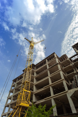Multi-storey residential building under construction and crane on a background of blue sky