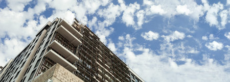 Panorama of a multi-storey residential building under construction and crane on a background of blue...