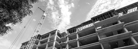 Black and white panorama of a multi-storey residential building under construction and crane on a...