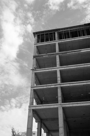 Black and white photo of a multi-storey residential building under construction and crane on a background of blue skyの写真素材