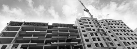 Black and white panorama of a multi-storey residential building under construction and crane on a background of blue skyの写真素材