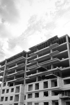 Black and white photo of a multi-storey residential building under construction and crane on a background of blue skyの写真素材
