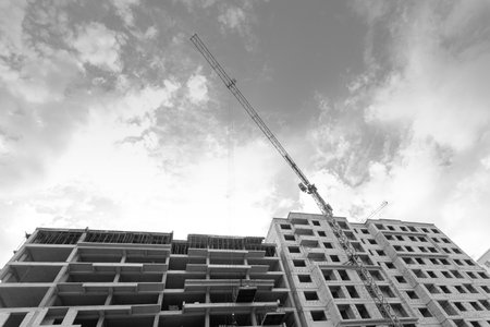 Black and white photo of a multi-storey residential building under construction and crane on a background of blue skyの写真素材