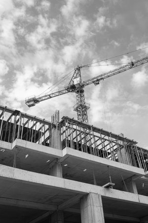 Black and white photo of a multi-storey residential building under construction and crane on a background of blue skyの写真素材