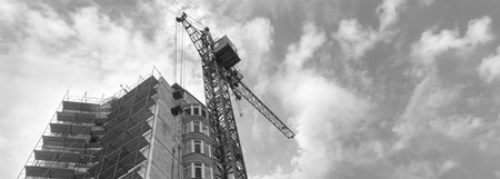 Black and white panorama of a multi-storey residential building under construction and crane on a...