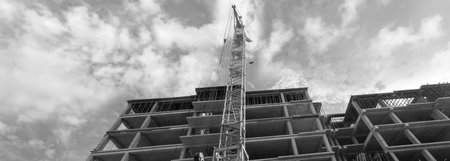 Black and white panorama of a multi-storey residential building under construction and crane on a...