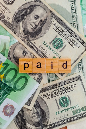 paid inscription on wooden cubes on the texture of us dollars and euro banknotes
