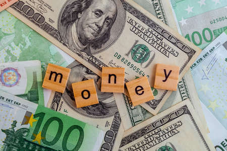 money inscription on wooden cubes on the texture of us dollars and euro banknotesの写真素材