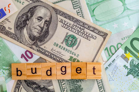budget inscription on wooden cubes on the texture of us dollars and euro banknotesの写真素材