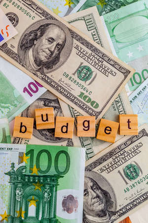 budget inscription on wooden cubes on the texture of us dollars and euro banknotesの写真素材