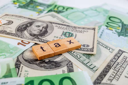 tax inscription on wooden cubes on the texture of us dollars and euro banknotesの写真素材
