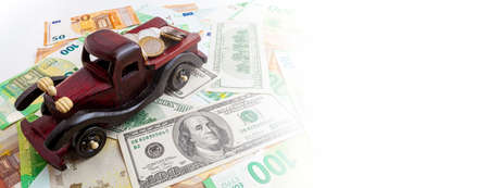 wooden car with coins on euro and dollars texture background panoramaの写真素材