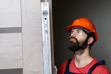 a worker with a drill in an orange helmet installs a door in the house