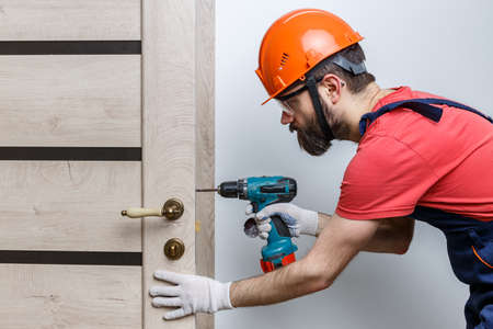 a worker with a drill in an orange helmet installs a door in the houseの写真素材