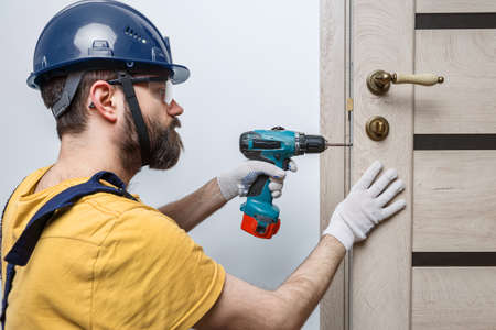a worker with a drill in an orange helmet installs a door in the houseの写真素材