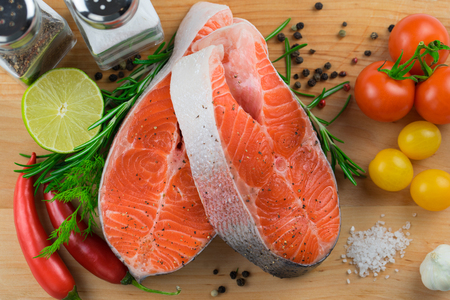 Close up of two raw fresh salmon steaks with vegetables and spices on a wooden background.の写真素材