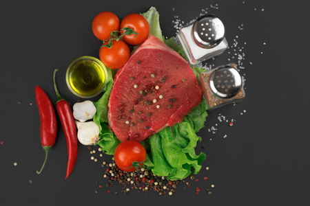 Top view of a raw beef steak with vegetables, greens and spices on a black background.の写真素材