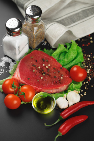 Raw beef steak with vegetables, greens and spices on a black background.の写真素材