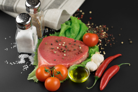 Raw beef steak with vegetables, greens and spices on a black background.の写真素材