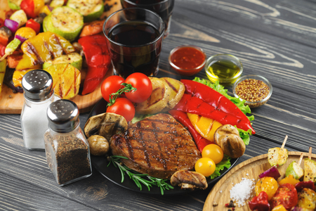 Grilled tasty beef steak with grilled potatoe, paprika, onions, mushrooms and vegetable skewers on a dark wooden background.の写真素材