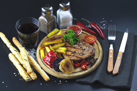 Beef steak with grilled vegetables and french fries on wooden cutting board put on black background.の写真素材