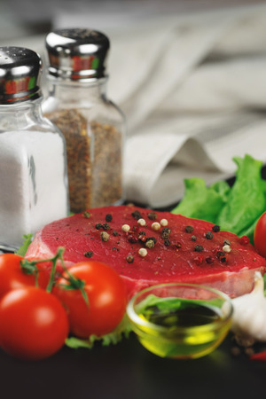 Raw beef steak with vegetables, greens and spices on a black background.の写真素材
