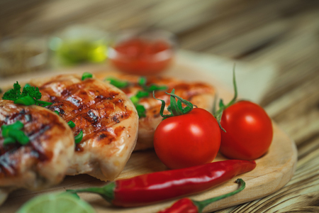 Close up of grilled chicken fillet with fresh vegetables, greens, and spices on wooden background.の写真素材