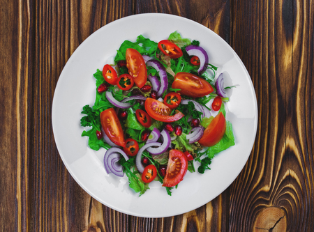 White porcelain plate with the salad of raw fresh vegetables on the dark wooden background. Healthy vegetarian snack.の写真素材