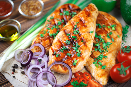 Close up of grilled chicken fillet with fresh vegetables, spices and sauces on wooden background.の写真素材