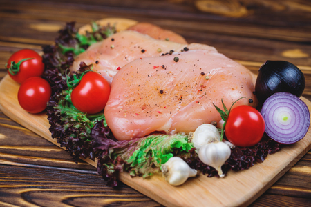 Close up of raw chicken fillet with vegetables and greens on the wooden background.の写真素材