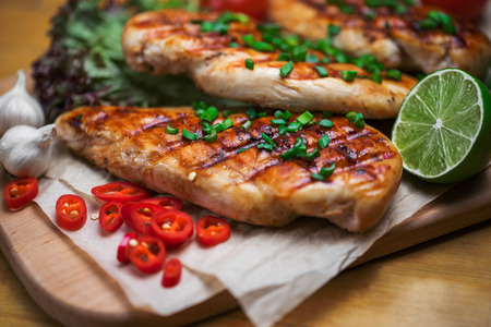Close up of grilled chicken fillet with fresh vegetables, greens, and spices on wooden background.の写真素材