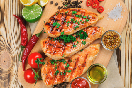 Top view of grilled chicken steaks with vegetables on wooden background.の写真素材