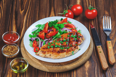 Grilled chicken fillet with vegetable salad, spices and sauces on wooden background.の写真素材