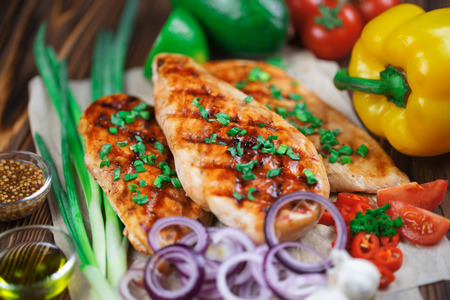 Close up of grilled chicken fillet with fresh vegetables, spices and sauces on wooden background.の写真素材