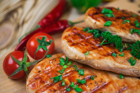 Close up of grilled chicken fillet with fresh vegetables, greens, and spices on wooden background.の写真素材