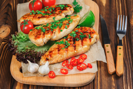 Griiled chicken fillet with cherry tomatos, salald, garlic, chili pepper, leek and lime on wooden background.の写真素材