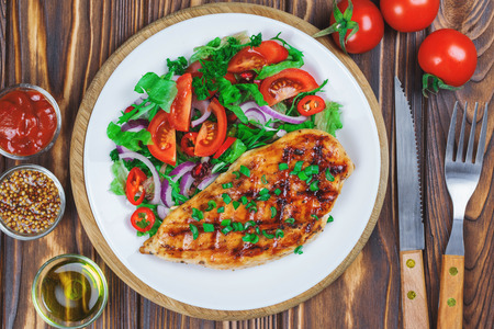 Grilled chicken steak with fresh vegetable salad on the wooden background. Top view.の写真素材