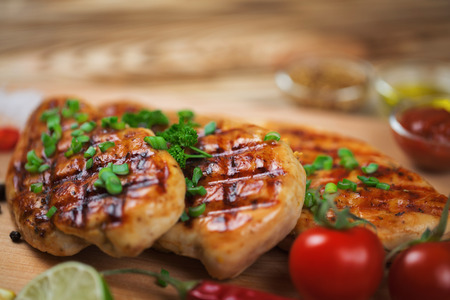 Close up of grilled chicken fillet with fresh vegetables, greens, and spices and sauces on wooden background.の写真素材