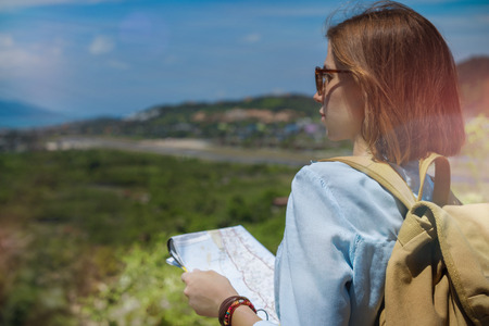 Young european female tourist with a backpack holding the map and looking at the valley from the viewpoint.の写真素材