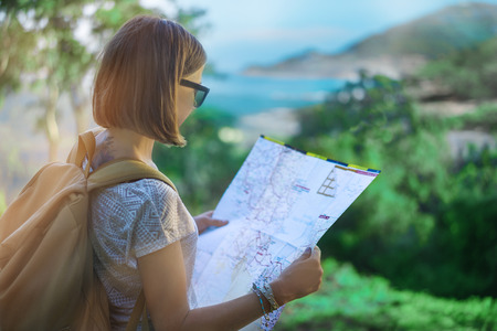 Young european female tourist with a backpack checking her map while standing on the view point with the scenic beauty landscape. Copy space for your text.の写真素材