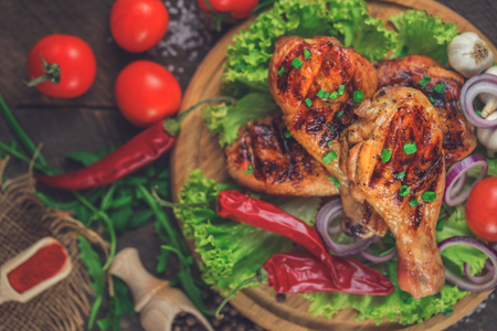 Top view of hot grilled chicken drumsticks with fresh vegetables on shabby wooden background.の写真素材